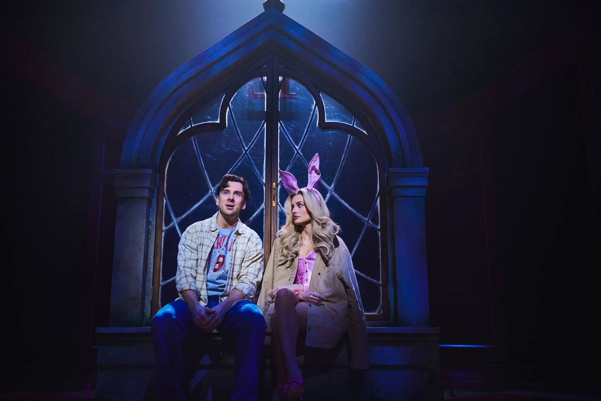 George Crawford as Emmett and Amber Davies as Elle Woods, still in bunny ears, sit on a Harvard bench at night